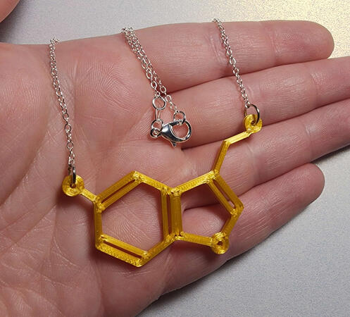 silver necklace with a gold pendant in the shape of a serotonin molecule