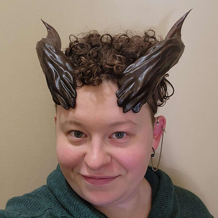 Two black ram-like horns; a pale person with curly hair is wearing them